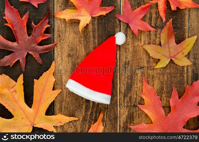 Red Santa Claus hat with dry leaf already on a wooden background