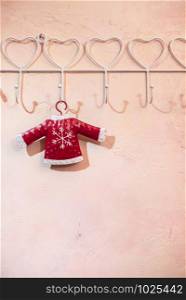 Red Santa Clause sweater with snowflake hooked on pink wall. White hanger with heart shapes. Love christmas concept. Copy space.