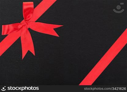 Red satin ribbon and bow gift box wrapping over black paper background