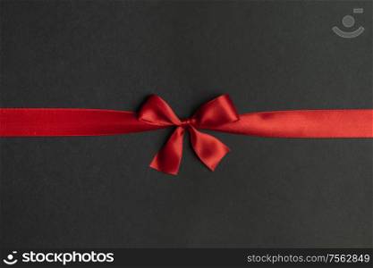 Red satin ribbon bow on black paper background. Red bow on black