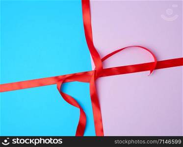 red satin ribbon on a colored background, imitation of tying and packing a gift