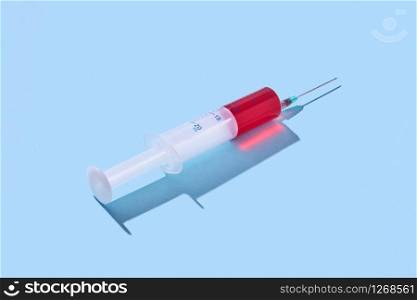 Red serum, vaccine in plastic syringe 20 ml for an intravenous injection on a pastel blue background with hard shadow, copy space.. Disposable syringe of red vaccine with hard shadow.