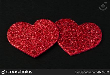 Red shiny hearts on black background. Brocade made hearts