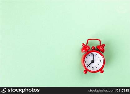 Red small alarm clock on light pastel green background with copy space, flat lay. Minimal style. Template for blog. Lifestyle. Time management concept, free time for important things.