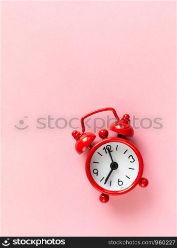 Red small alarm clock on pastel pink background with copy space, flat lay, macro. Minimal style. Time management concept. Vertical.
