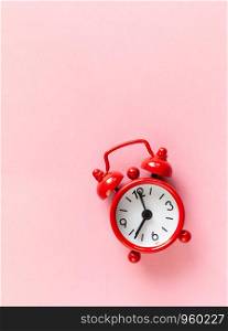 Red small alarm clock on pastel pink background with copy space, flat lay, macro. Minimal style. Time management concept. Vertical.