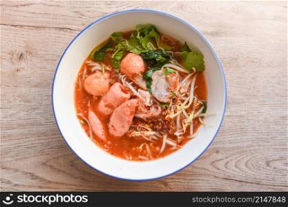 Red soup noodle pork with red roasted pork and bean sprout vegetable in soup bowl on wooden table, top view Thai and China Asian food