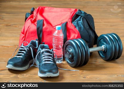 Red sports bag and sneakers near a heavy dumbbell on a wooden floor