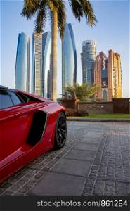 Red sports car under palm tree in front of skyscrapers