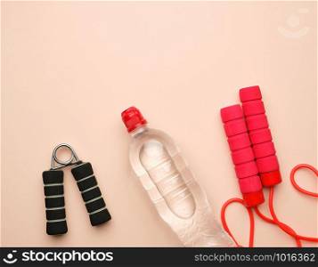 red sports rope for jumping and cardio load, transparent bottle on a beige background, close up