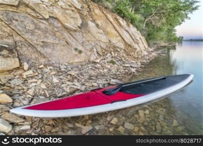 red stand up paddleboard with a paddle on a lake shore with a rocky cliff -Boedecker Reservoir near Loveland, Colorado