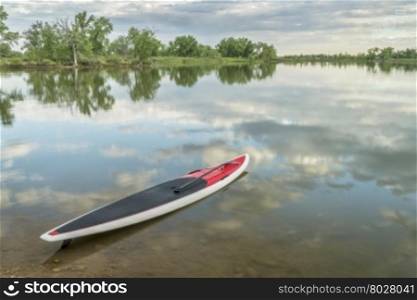 red stand up paddleboard with a paddle on calm lake ready for paddling workout - Arapaho Bend Natural Area, Fort Collins, Colorado