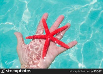Red starfish in human hand floating in turquoise tropical beach