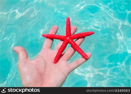 Red starfish in human hand floating in turquoise tropical beach