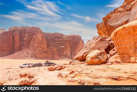 Red stones and rocks of Wadi Rum desert with cars in the background, Jordan