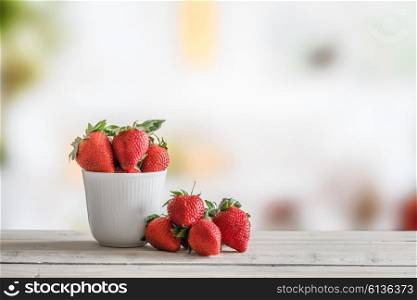 Red strawberries in a white cup on a wooden table