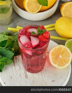 red strawberry lemonade in a glass on a round white wooden board, yellow lemons are behind, top view