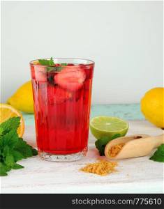 red strawberry lemonade in a glass on a white wooden board, yellow lemons are behind