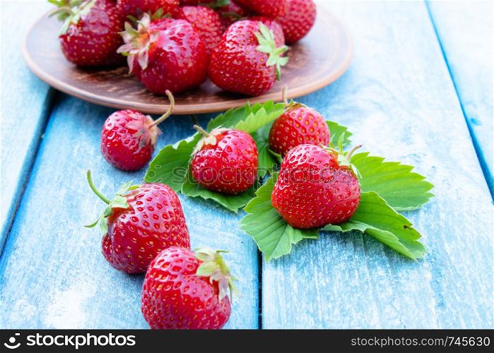 red strawberry lies on green leaves against the background of blue old boards. copy space. red strawberry lies on green leaves against the background of blue old boards.