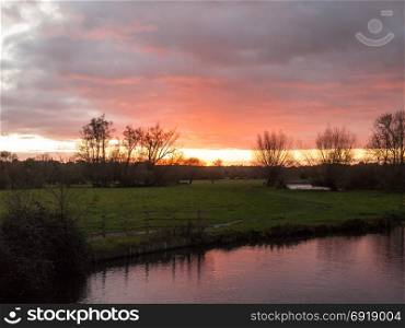 red sun setting sky dramatic autumn over empty open green countryside night dark lake; essex; england; uk