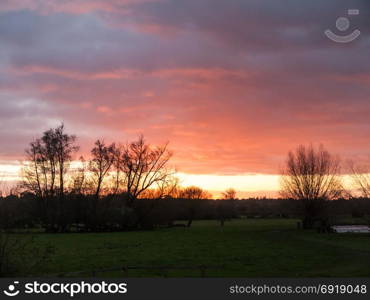 red sun setting sky dramatic autumn over empty open green countryside night dark; essex; england; uk