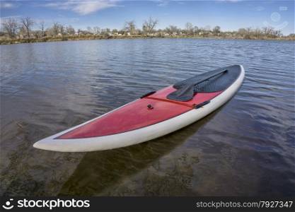 red SUP paddleboard with a paddle on a lake shore ready for paddling, spring time in Colorado