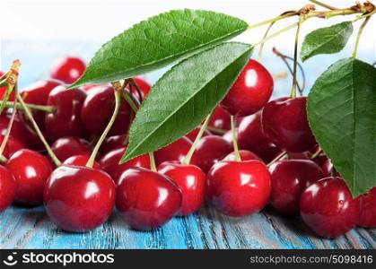 Red sweet cherry and green leaves on a blue wooden background