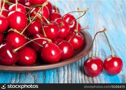 Red sweet cherry in a clay dish on a blue wooden background