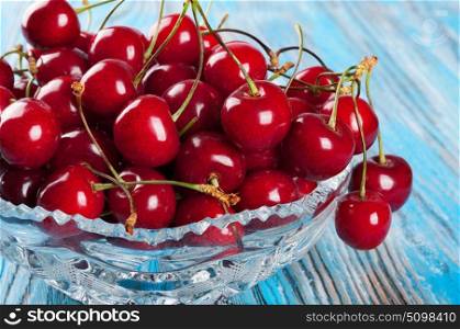 Red sweet cherry in crystal vase on a blue wooden background
