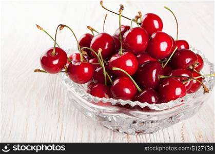 Red sweet cherry in crystal vase on a wooden background