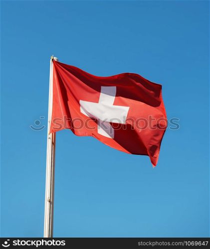 Red Switzerland national flag on pole waving against clear blue sky