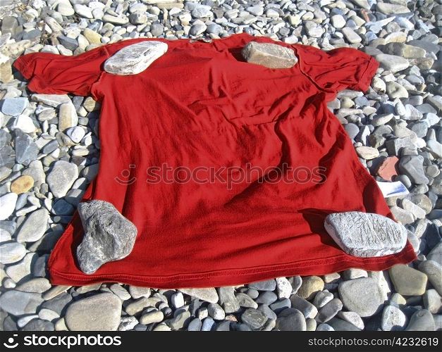 Red t-shirt lay on the shore under four stones