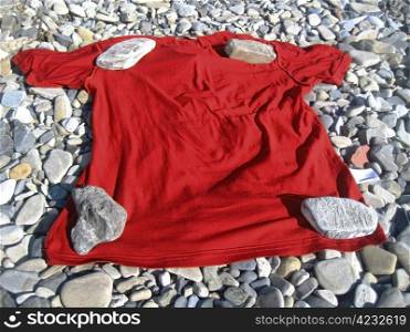Red t-shirt lay on the shore under four stones