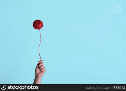 Red thread ball, floating like a balloon and a woman hand holding it. Weird childhood concept. Minimal style knitting context.