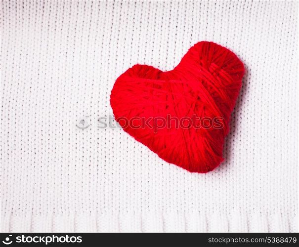 Red thread heart over knitted white textile. Valentine background