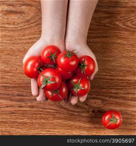 red tomatoes in hands on wooden background