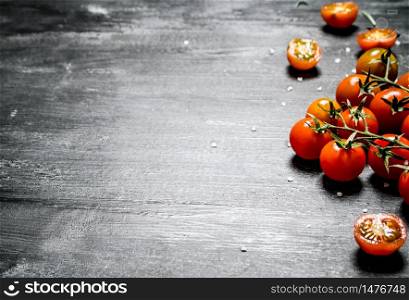 Red tomatoes on a branch. On black rustic background.. Red tomatoes on a branch.