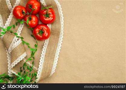 Red Tomatoes on brown craft paper background with natural colored burlap ribbon top view, copy space, Vegan, vegetarian,healthy food,vegetables concept space for text. Red Tomatoes on brown craft paper background with natural colored burlap ribbon top view, copy space, Vegan, vegetarian,healthy food,vegetables concept