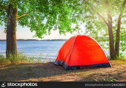 Red tourist tent on the lake under the bright sun in summer. Red tourist tent on lake under bright sun in summer