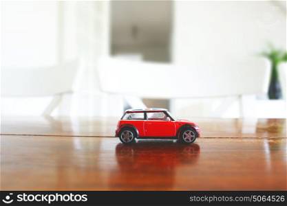 Red toy car in red color on a wooden table in a bright indoor environment