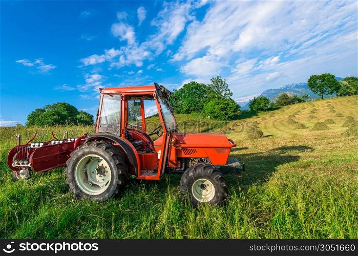 Red tractor in a mountain meadow with hay bales handmade