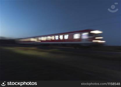 Red train in motion with light at windows, in the evening. Traveling by night. Train travel. Blur motion train. Eco-friendly public transport.