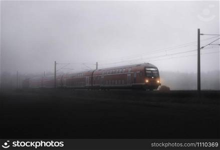 Red train traveling through fog, in german countryside scenery, near Schwabisch Hall, Germany. Eco-friendly public transportation on railway tracks.