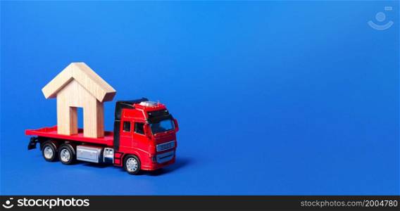 Red truck carrier with a house figure on a blue background. Cargo transportation and delivery service. A moving company. Infrastructure and logistics industry. Relocation of buildings and monuments.