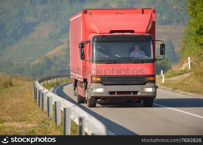red truck driving on asphalt road in a rural landscape