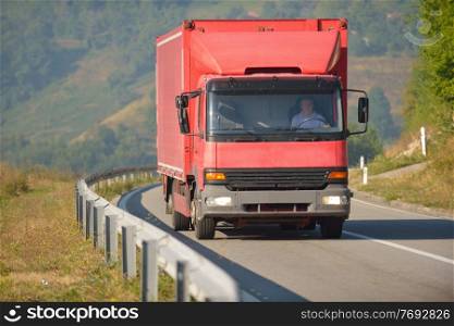 red truck driving on asphalt road in a rural landscape