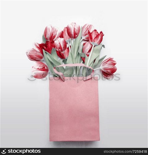 Red tulips bouquet in paper shopping bag on light gray background. Festive spring flowers bunch. Floral gift composing. Springtime holiday , greeting or sale concept. Copy space for your design