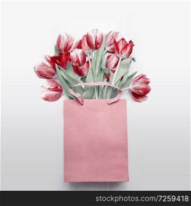 Red tulips bouquet in paper shopping bag on light gray background. Festive spring flowers bunch. Floral gift composing. Springtime holiday , greeting or sale concept. Copy space for your design