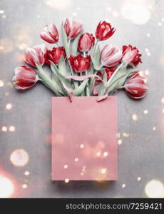 Red tulips in paper shopping bag. Festive spring flowers bunch with bokeh. Floral gift composing. Springtime holiday and greeting concept