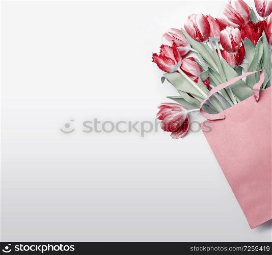 Red tulips in paper shopping bag on light gray background. Festive spring flowers bunch. Floral gift composing. Springtime holiday , greeting or sale concept. Copy space for your design